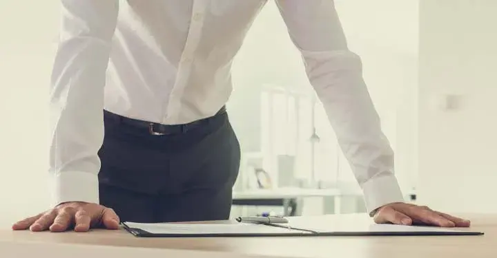 Man with hands planted on table leaning over an open binder