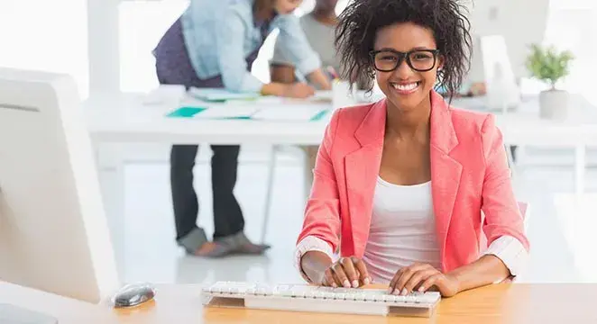 Smiling woman typing at laptop in pink blazer in office space