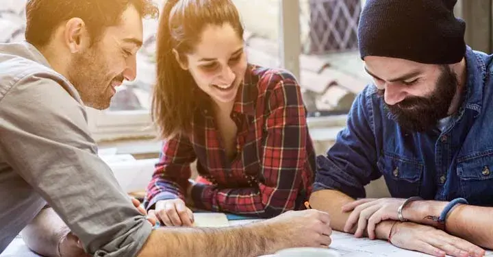 Three casually dressed hipsters laugh while signing documents