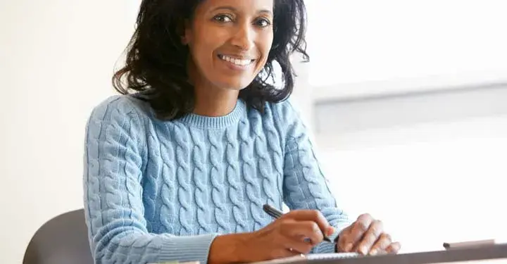 A woman in a blue sweater smiling and signing a document