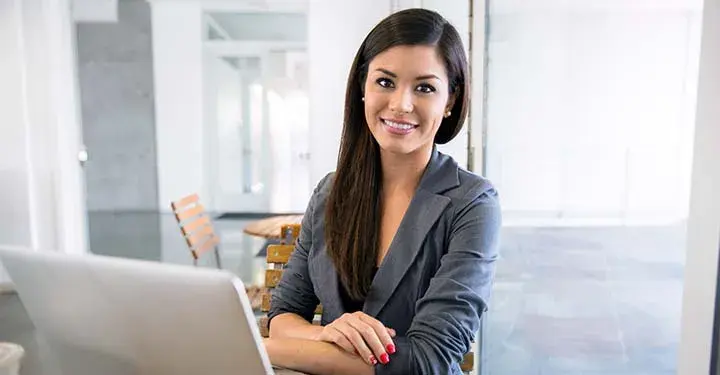 Woman with crossed arms smiling behind her open laptop