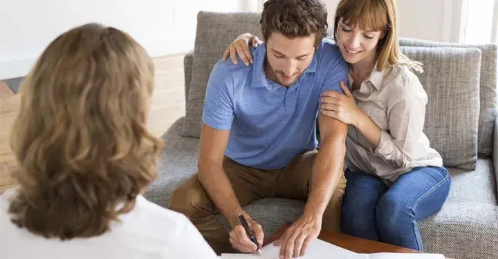 Couple on gray couch signing document in front of woman