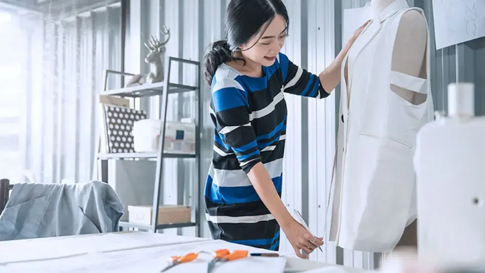 A dress designer measures fabric on a dress dummy.