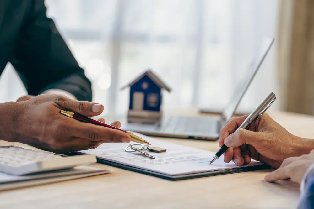 A tenant returns keys to the landlord as they sit on opposite sides of a desk. They each have a pen in hand.