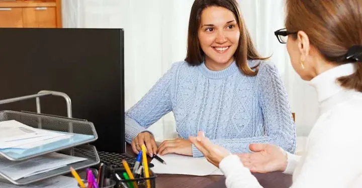 Two women in an office talking at a desk