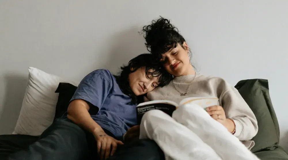 Two people in a common law marriage snuggle on a bed while reading a book