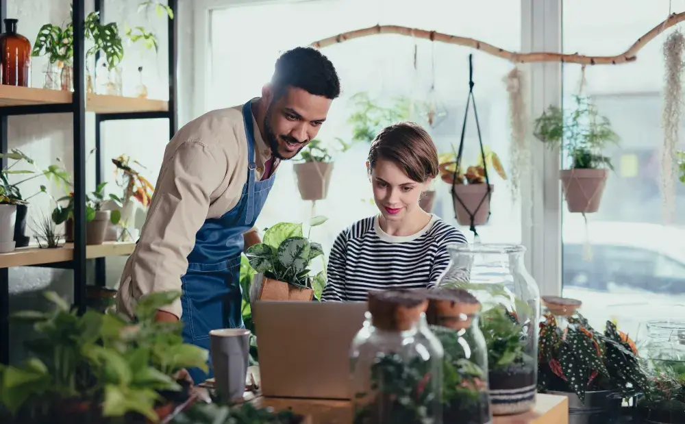 A man and woman in their plant shop look at their business expenses online. With an LLC, you can pay federal taxes through your personal income tax return or be taxed as a corporation.