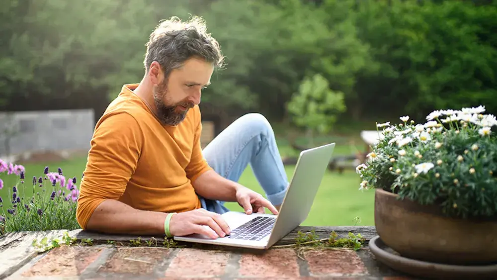 A businessman sits outside working on his open laptop as he contemplates procuring consultation and support services.