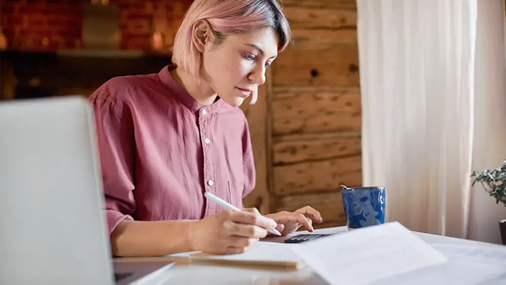 A woman sitting at a desk takes notes on how to start an LLC in New York.