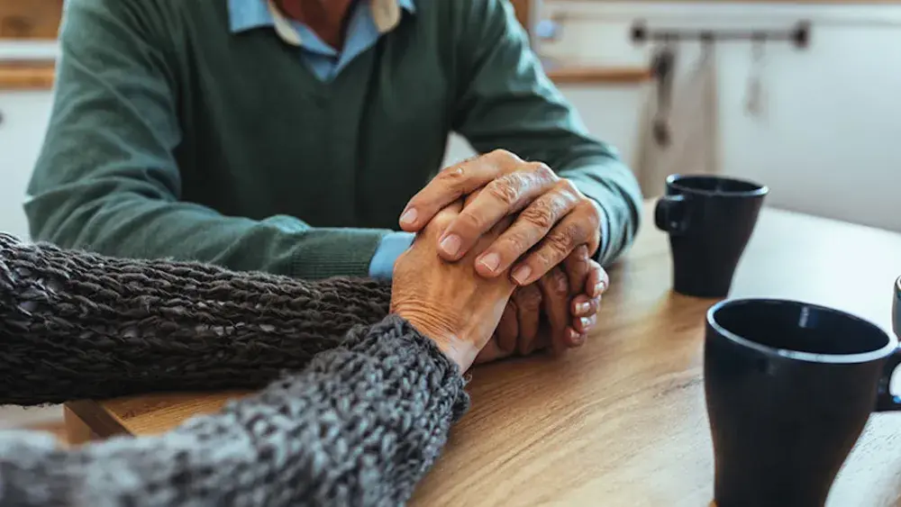 An elderly couple holds hands at a kitchen table. Ongoing trust management is crucial to ensure the trust serves its intended purpose and provides financial security for your beneficiaries.