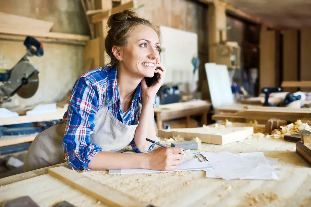 A woman leaning over a table in a workshop talks on the phone to get information about starting her California LLC.