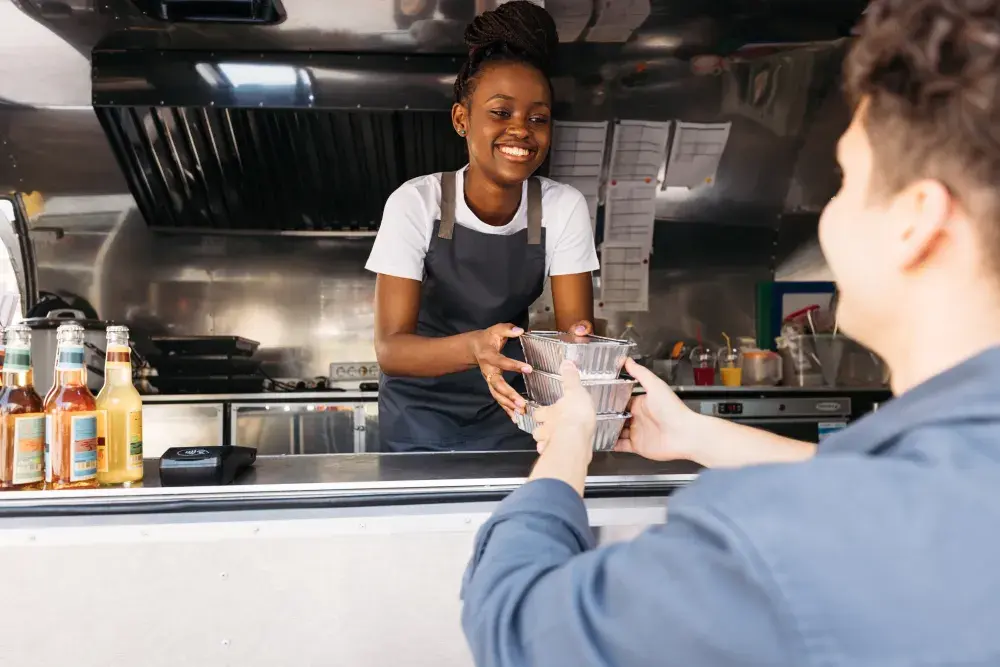 A woman in a food truck hands containers of foods to a customer. To form a Texas LLC, it is necessary to select a unique name, file documents with the Secretary of State, appoint a registered agent, and obtain an EIN.