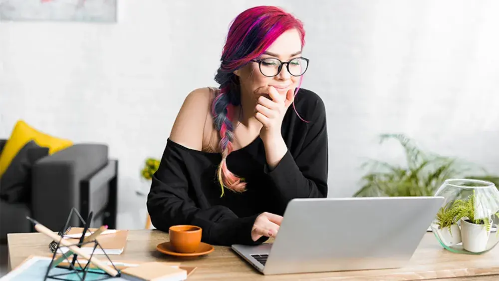 A woman with multicolored hair sits at her desk reading her open laptop. The state of Florida will issue a certificate that confirms an LLC formally exists after documents are submitted and approved.