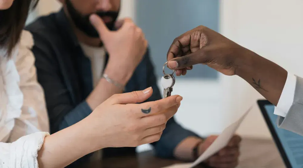 A woman who is standing next to a man and accepting house keys. A property was transferred to her following the death of a loved one.