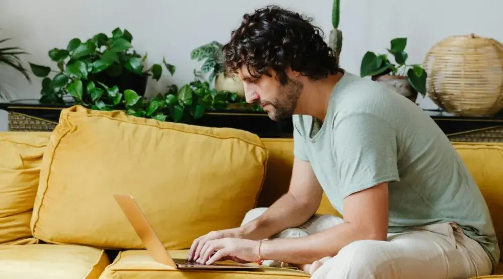 A man sitting on a yellow couch and conducting an Idaho business search on his laptop