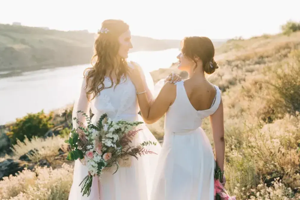 Two women dressed in white bridal gowns exchange wedding vows on a scenic hill overlooking a river. the process or task of creating your own prenuptial agreement can be an important step toward establishing a solid relationship with your spouse. 