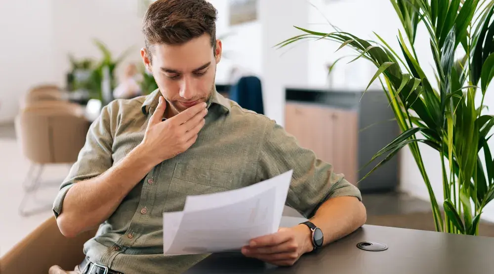 A man carefully reading through a contract containing a sunset clause at a table and considering hiring an attorney