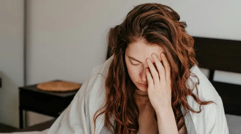 A red-haired woman sits on her bed and holds her head; she looks stressed. Depending on the source of your emotional distress, you may be able to file a lawsuit.