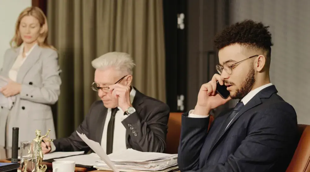 A man sits at a court hearing for a damages suit and talks on the phone while his lawyer reviews documents.