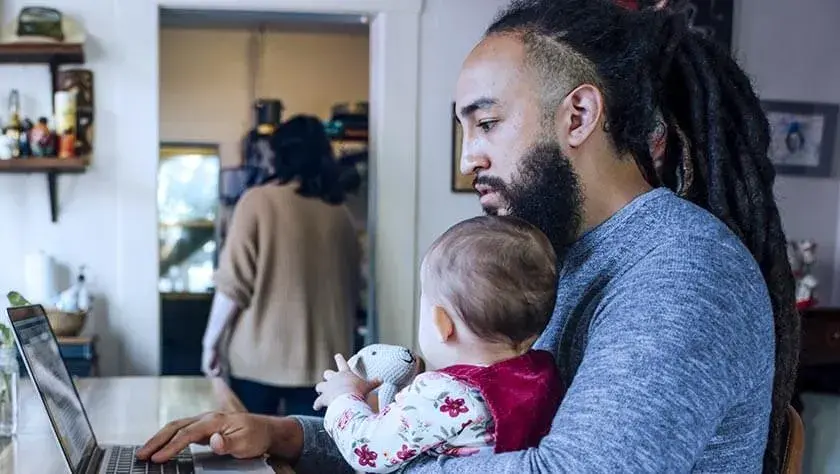 man-holding-baby-using-laptop-at-home in the living room