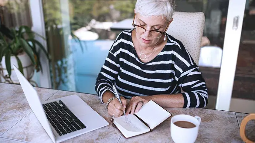 Senior woman taking notes from laptop