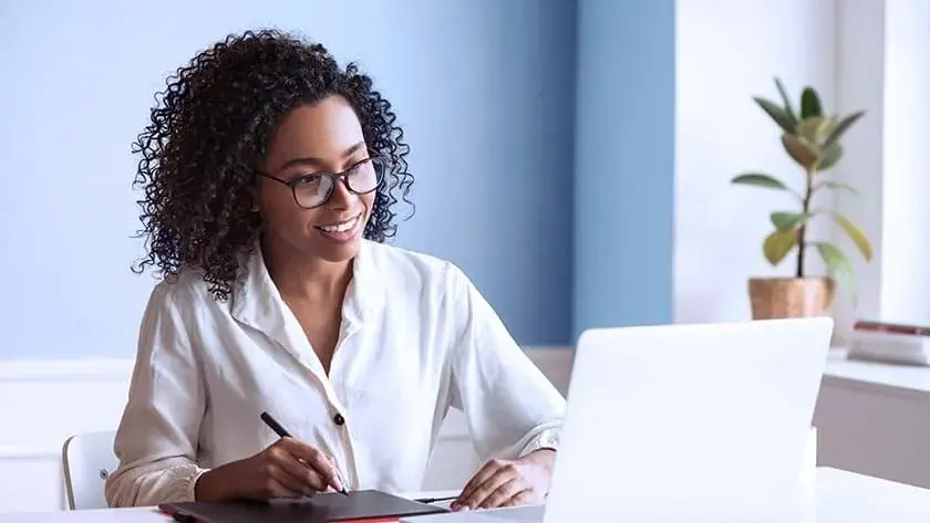 smiling-woman-sits-at-desk-using-stylus-wacom-tablet wearing a white blouse