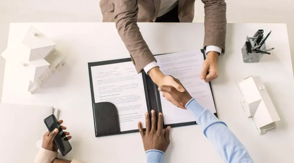 Two people sit across from one another and shake hands over a contract. When you can't agree with your joint owner about what to do with a property, a partition action can force a result.