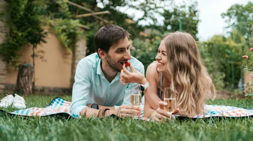 A woman feeds her fiance a berry as they lie on a blanket outdoors and sip champagne. Deciding whether a prenup is appropriate for you and your spouse-to-<a href=