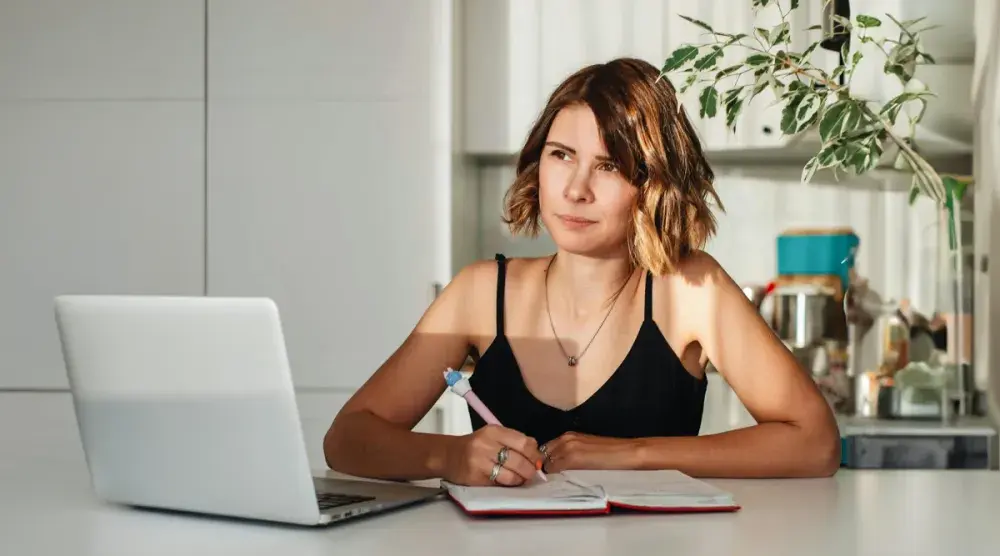 An adult woman sitting at a counter in front of a laptop researching what questions she should ask a copyright lawyer