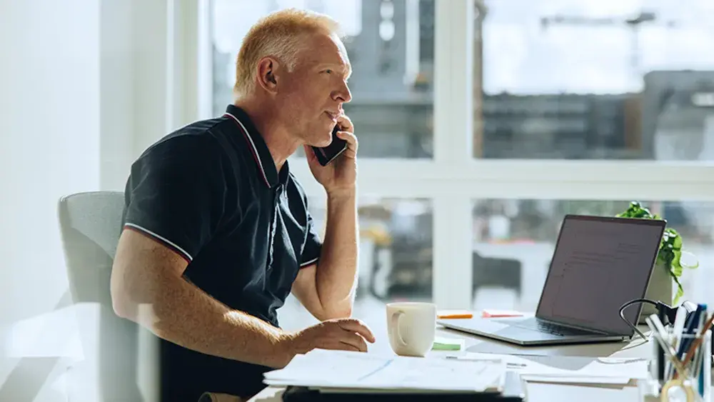 A man sits at his desk in an office and talks on the phone with an estate planning attorney.