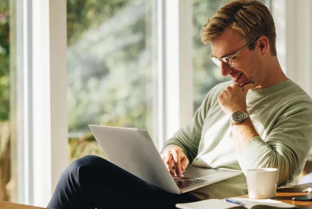 A smiling man seated sideways at a desk looks at his open laptop as he does a name search for his California business 