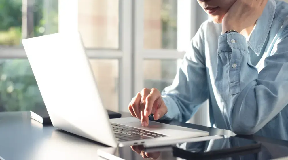 A person in a blue shirt works on a laptop computer. If you're thinking of starting a new business in Arizona, you can conduct a business name search for free via the Secretary of State's website.