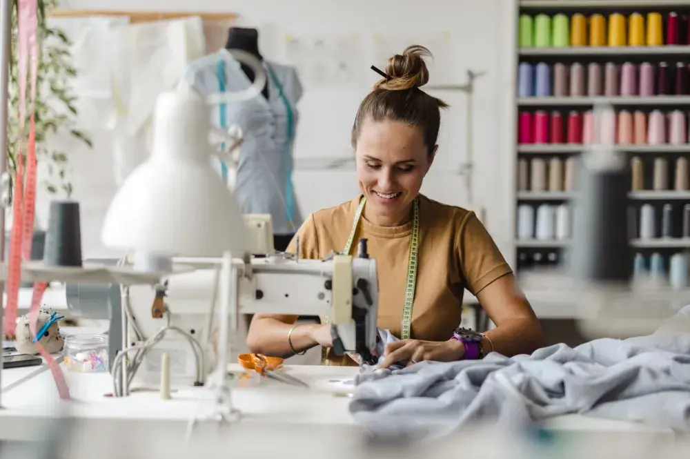 A tailor works at her sewing machine in her shop. Some things she should consider when choosing a business entity: start-up costs, government regulation, liability protection, and tax implications.