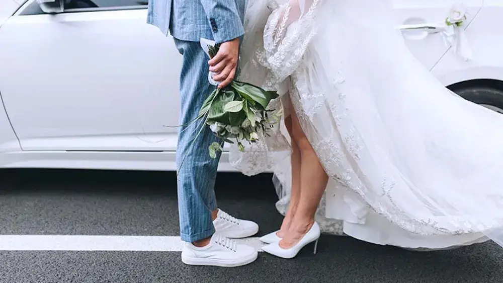 A bride and groom stand in front of their limo. Prenups are a practical tool that benefits married couples from all walks of life.