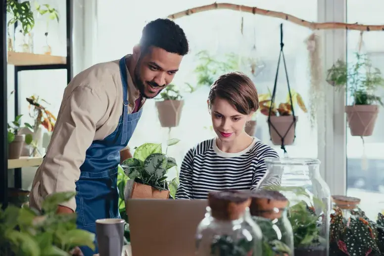 A man stands next to a woman seated at a desk while they both look at the screen of an open laptop computer discussing how to go paperless. Earth Class Mail can help with this process.