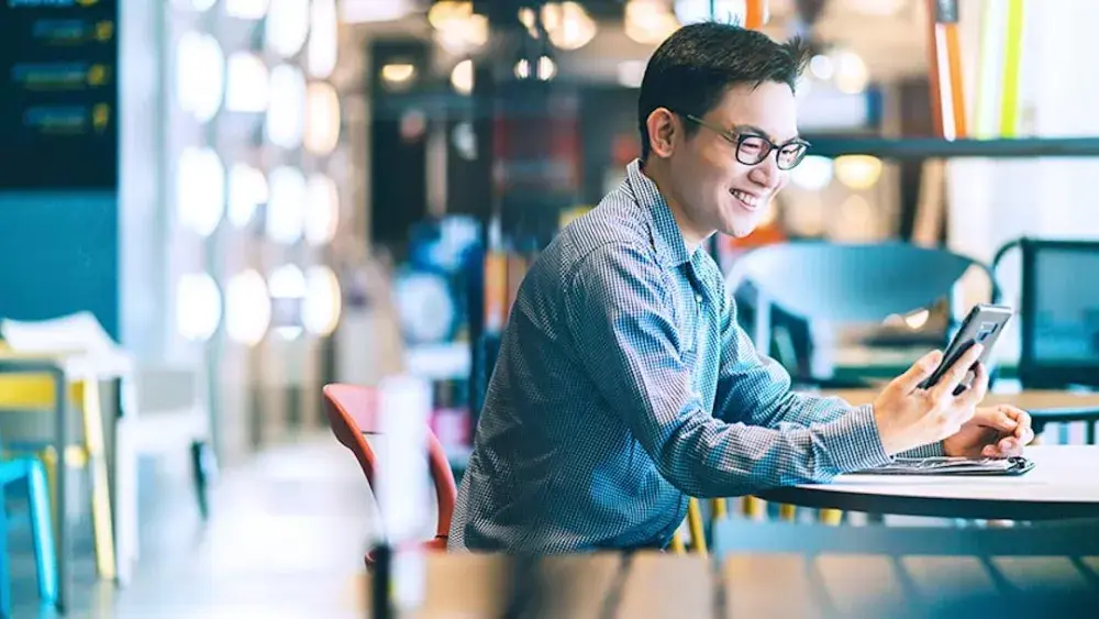 A man sits at a table in a coffeeshop, looking at his smartphone and reading about Texas living trusts. The living trust is a valuable tool for estate planning in Texas. 