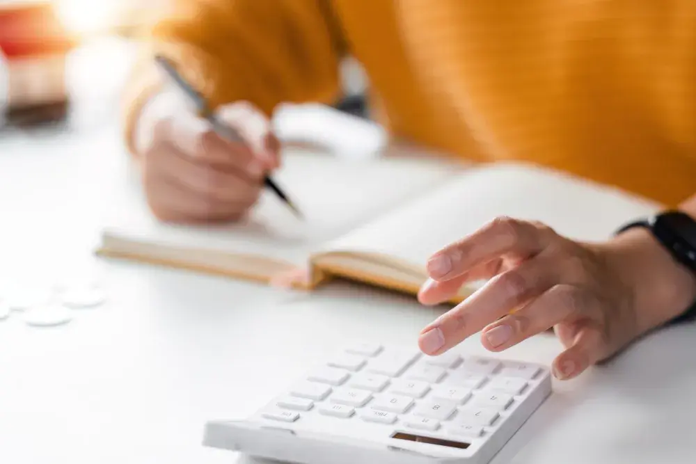 A person seated at a desk uses a large calculator while writing in a notebook using the accrual accounting method..