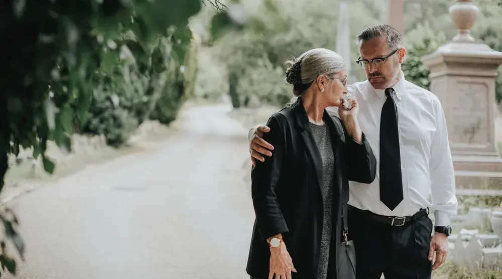 A man wraps his hand on a woman's shoulder as they walk through a cemetery. Learn what and what not to do after a loved one has passed away and you need to settle their legal affairs. 