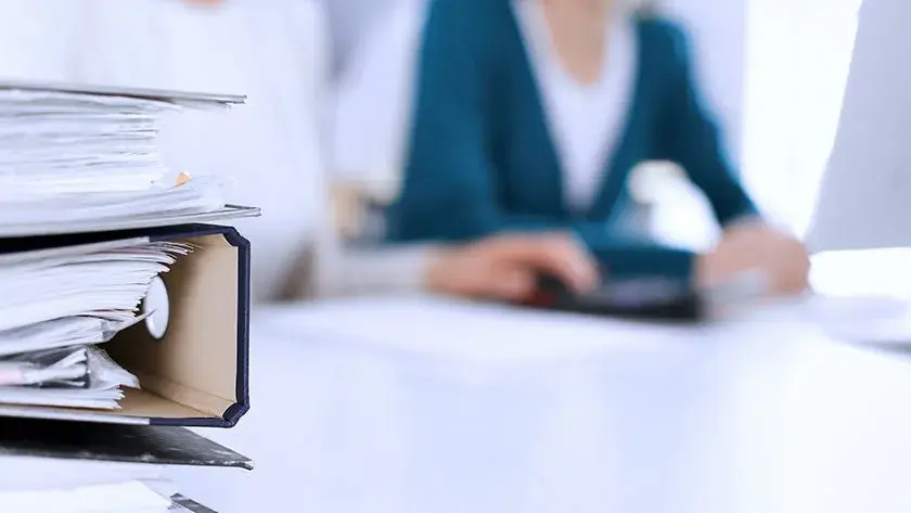 binders of tax paperwork on a desk with people in the background 