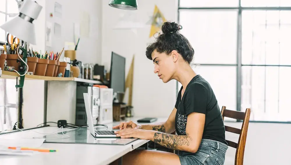 A woman sits at a desk looking at her open laptop computer as she reads about what kinds of material can be copyrighted.