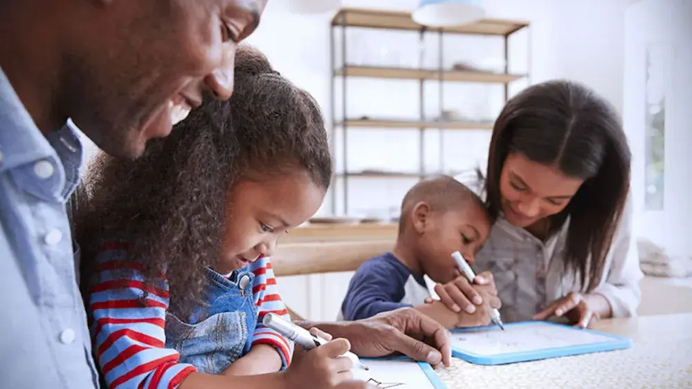 A man and woman sit at a table and help two children with homework. A living trust guides your assets from your ownership to your beneficiaries. It is an estate planning tool you create during your lifetime.