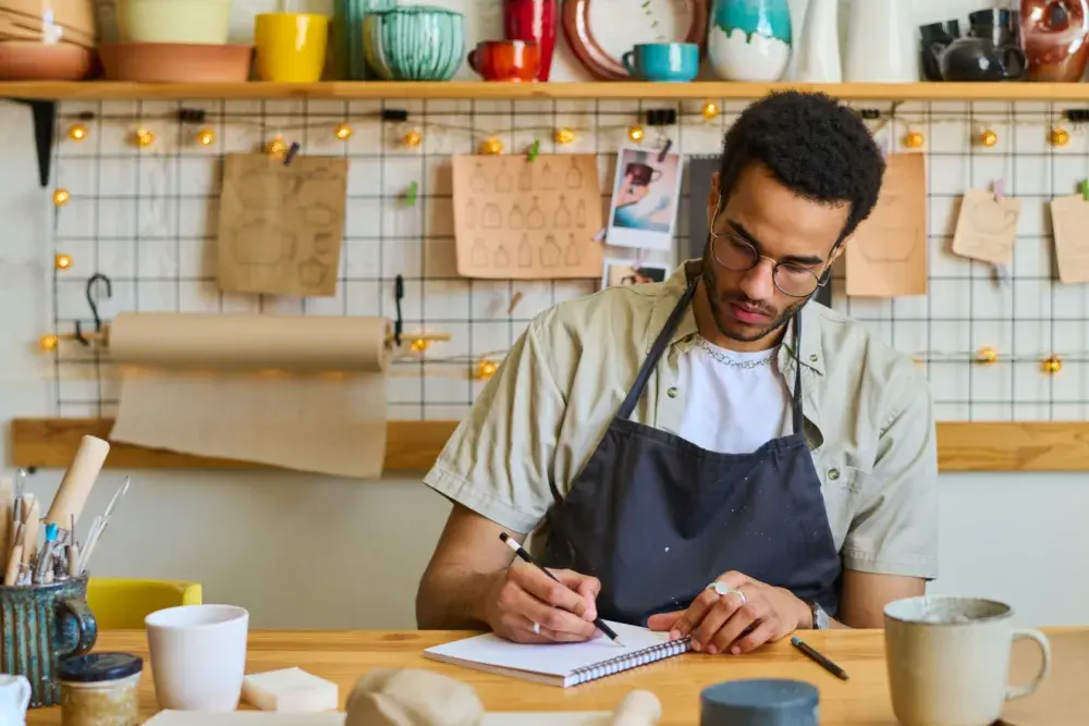 A potter sketches an idea in his notebook while working at his shop. 