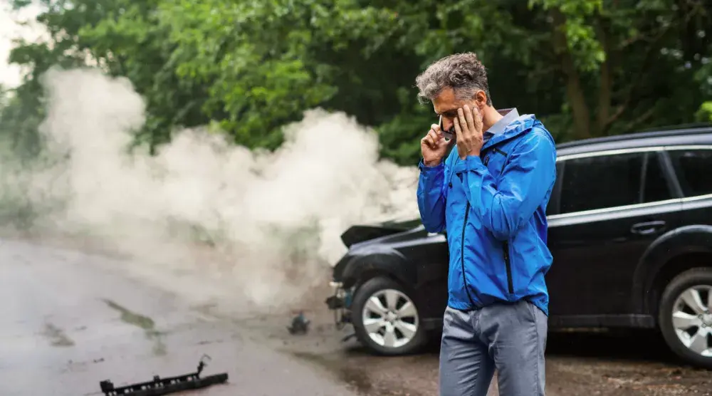 A man talks on his cell phone next to a car with smoke coming out. For serious car accidents, consider hiring an attorney to represent you.