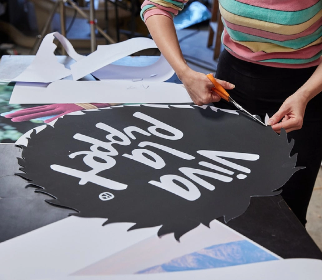 Person in striped rainbow long sleeve cutting out a paper logo